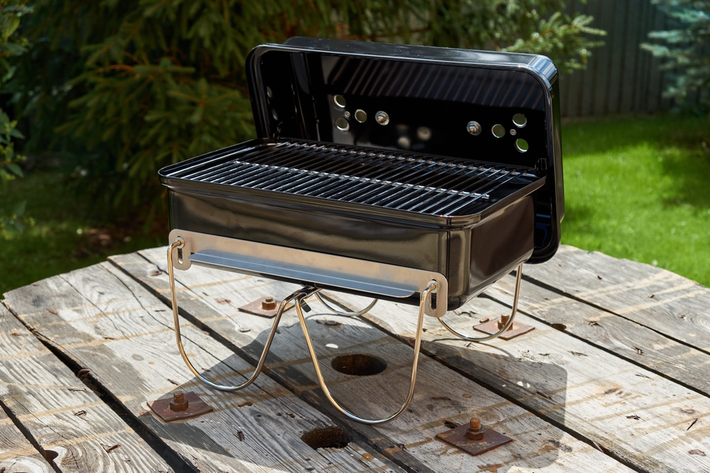 A Weber portable charcoal BBQ open on top of a wooden table outside.