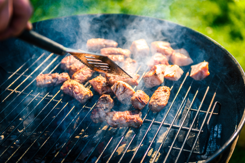 A person grilling meat on a Weber BBQ.