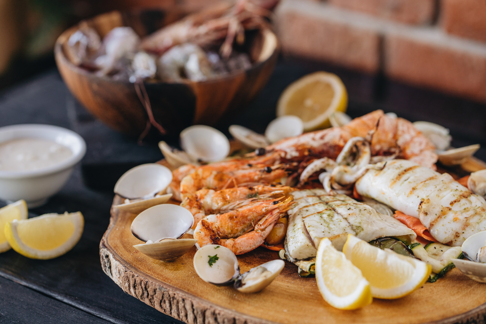 A range of seafood that has been barbecued displayed on a wooden board with lemon wedges.