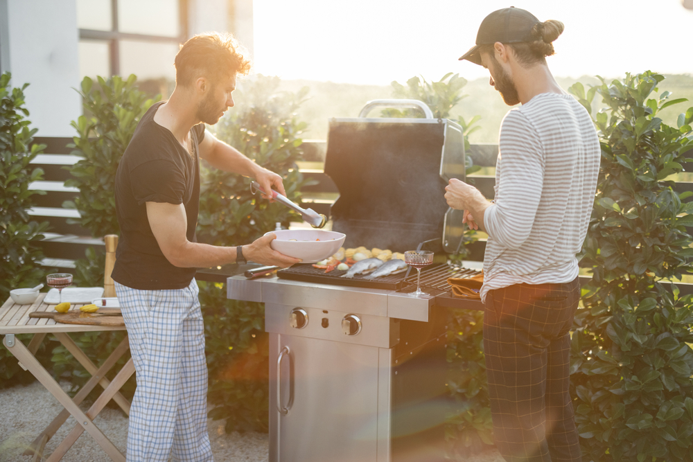 Two men cooking seafood and vegetables on a backyard BBQ in the afternoon light.
