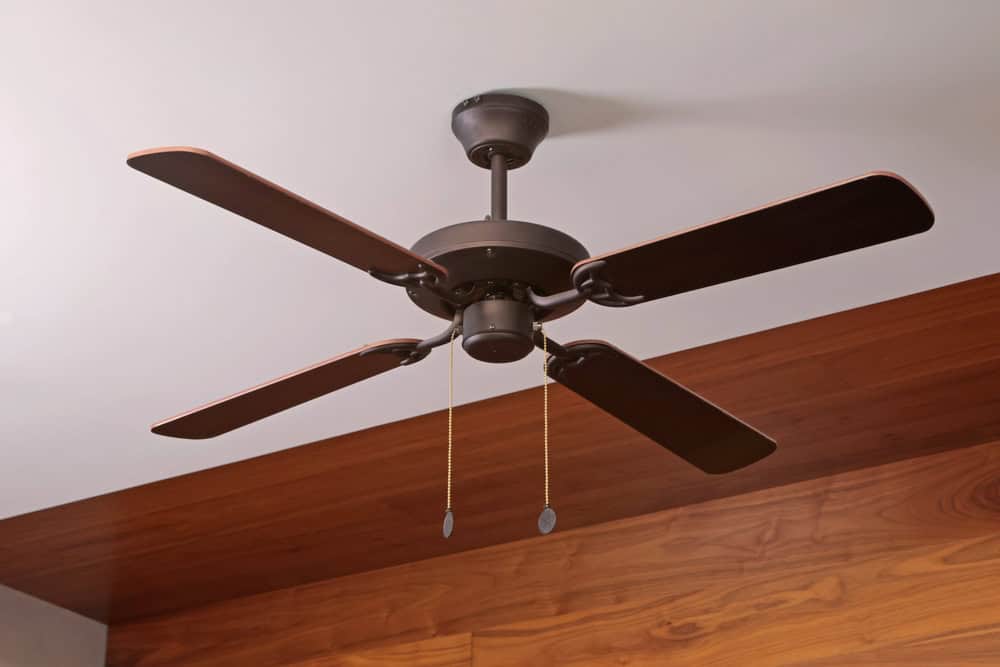 A dark ceiling fan on a wooden and white ceiling.