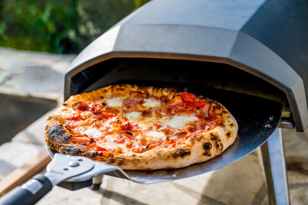 A crispy golden pizza being pulled out of a gas pizza oven.