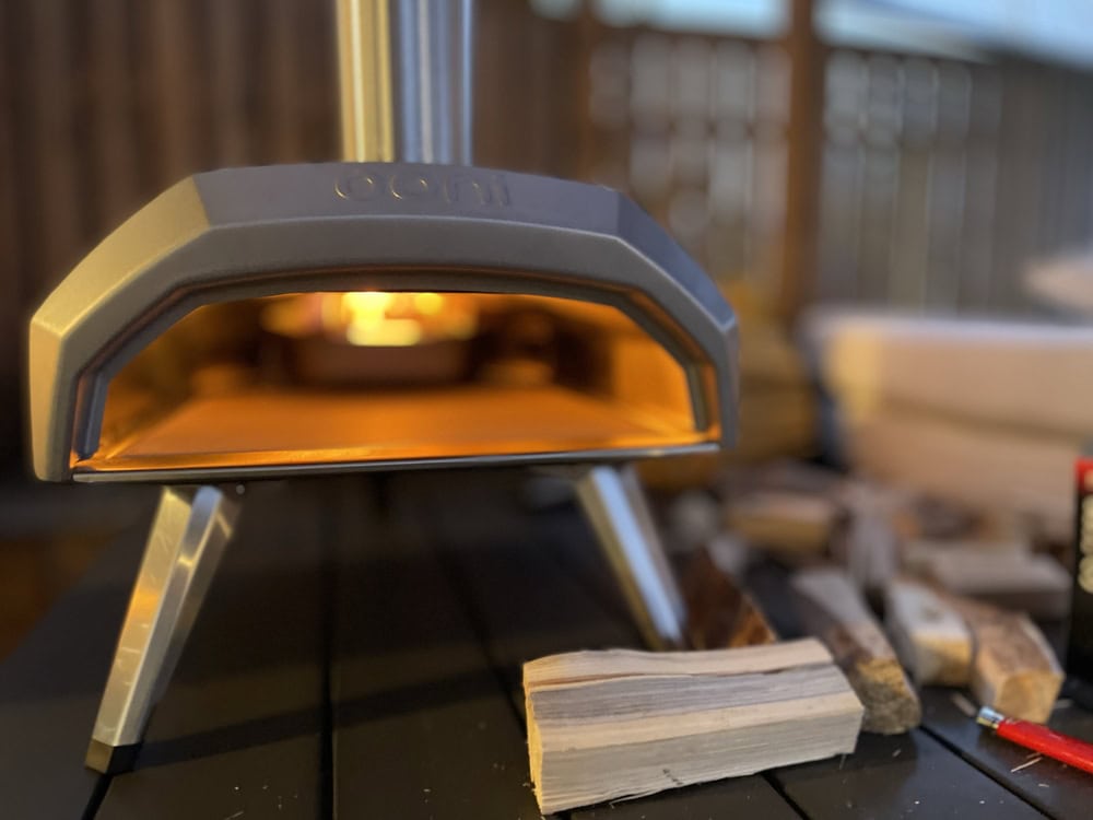 A woodfired pizza oven heating up with a piece of unused wood in front.