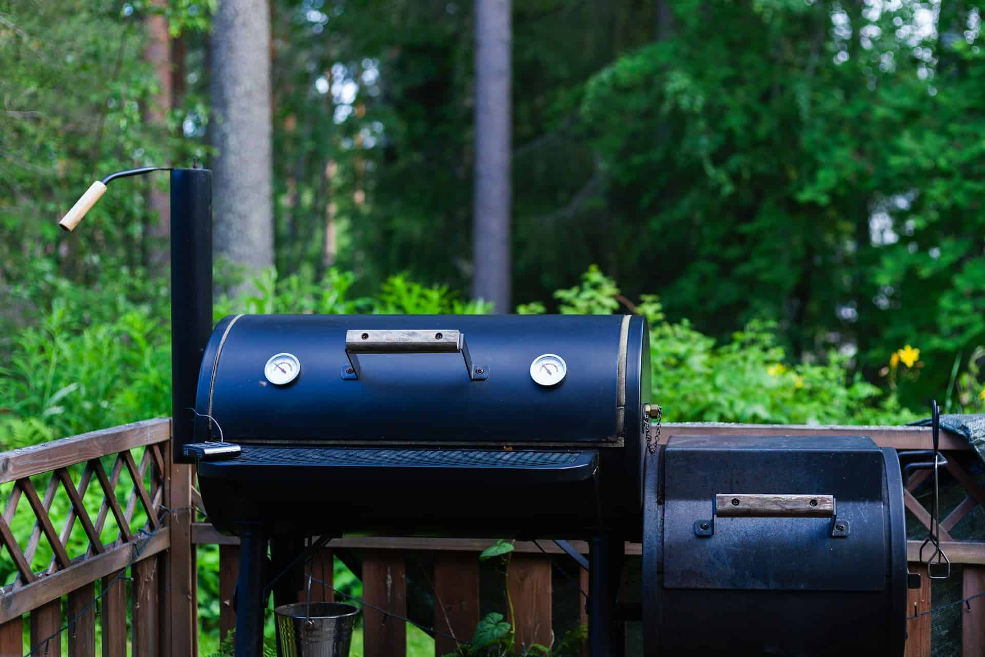 A smoker BBQ outside on a back balcony in a serene backyard. 