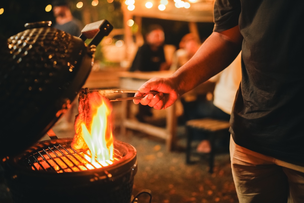 A person cooking a piece of meat on the BBQ while experiencing a flare-up.