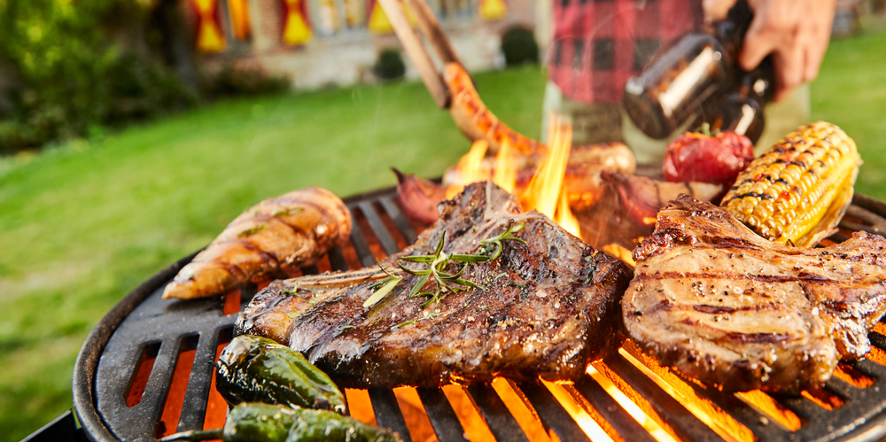 Various cuts of meat and vegetables grilling on a BBQ.