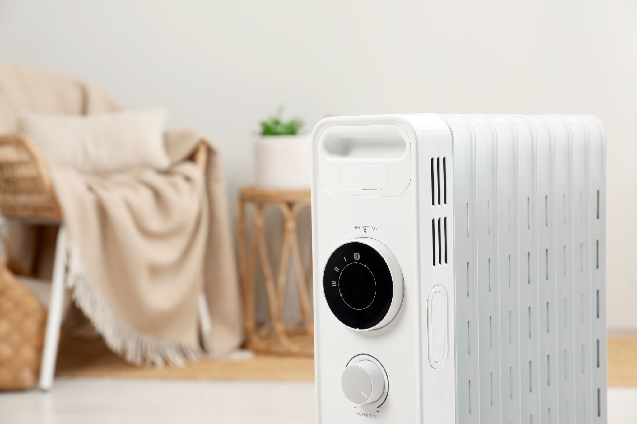 alt text: A close-up of a modern white electric oil-filled radiator heater positioned in a cozy, neutral-toned room.