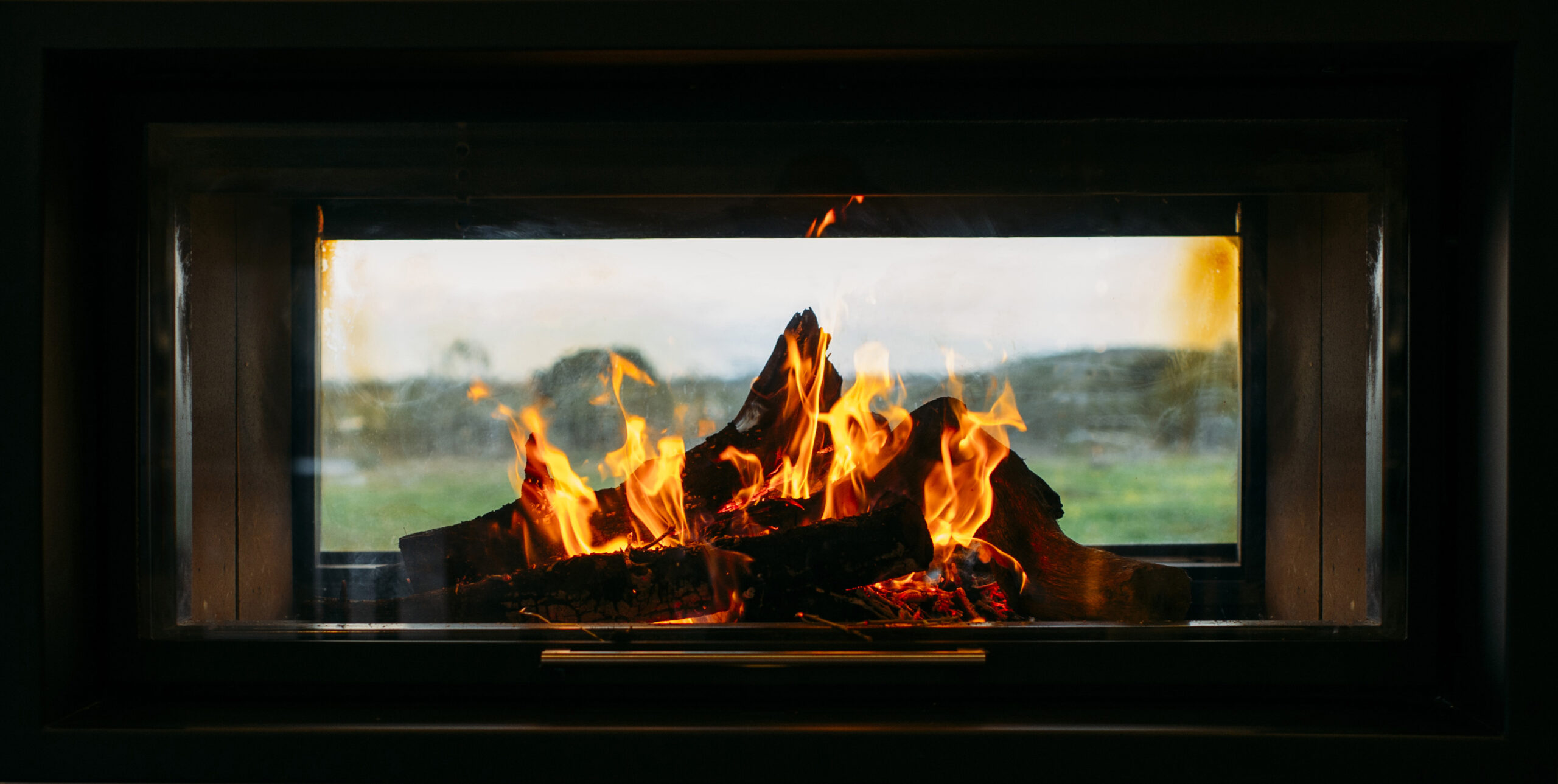A close-up view of a modern wood-burning fireplace through a glass pane, showcasing the warm glow and crackle of burning logs.