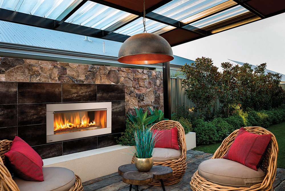 A Regency HZ042 wide-angle outdoor gas fireplace installed on a tiled feature wall next to comfortable woven patio armchairs.