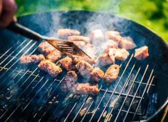 A person grilling meat on a Weber BBQ.