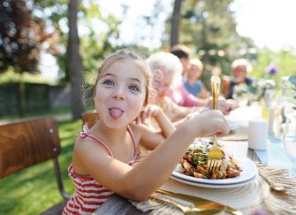 A little girl poking her tongue out while sitting at the backyard BBQ table.