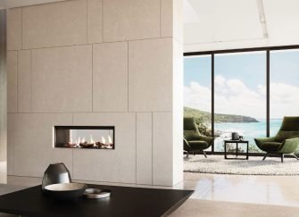 A modern double-sided gas fireplace built into a minimalist stone feature wall separating two light-filled living zones with coastal views.