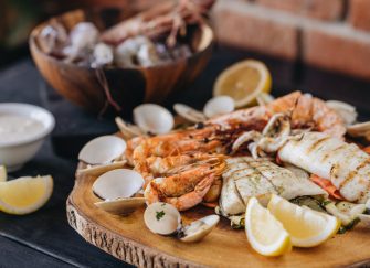 A range of seafood that has been barbecued displayed on a wooden board with lemon wedges.